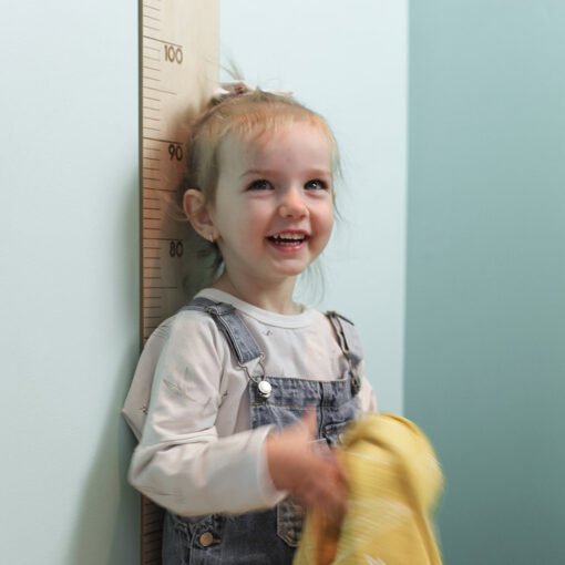 petite fille avec sa doudou jaune pose devant l'échelle de croissance