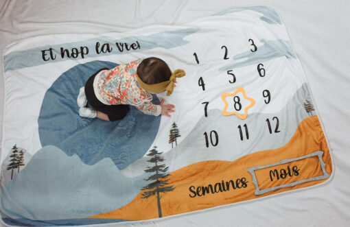 photo mensuelle 8 mois d'une petite fille qui rampe sur couverture à motif de montagnes
