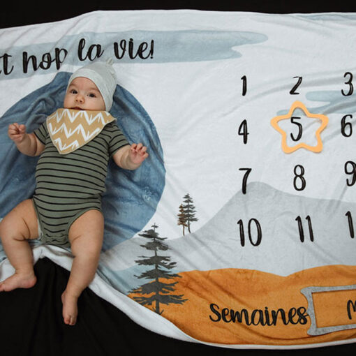 photo mensuelle 5 mois d'un petit garçon portant bonnet gris et bavoir jaune et blanc sur couverture à motif de montagnes
