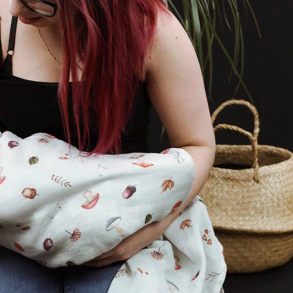 bébé emmailloté avec la mousseline au motif d'automne dans les bras de maman