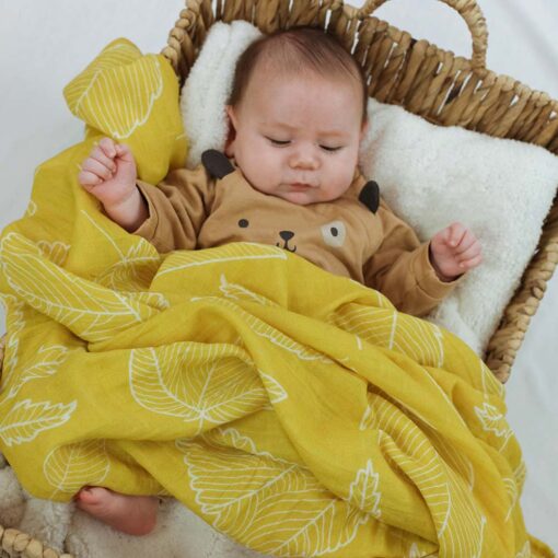 bébé dans un panier en osier avec mousseline jaune au motif de feuilles