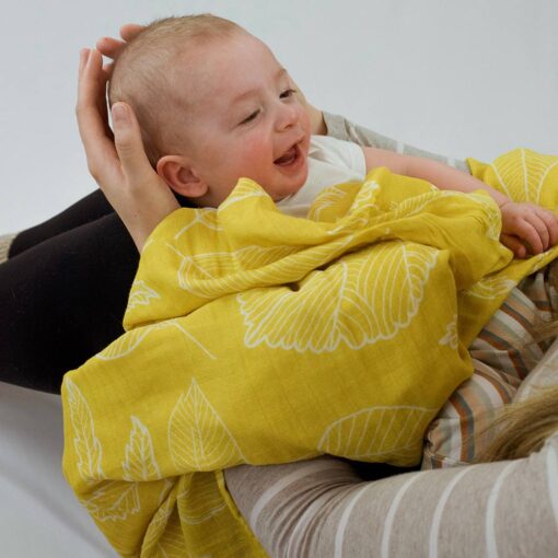 bébé avec sa mousseline jaune au motif de feuilles fait des sourires à sa maman