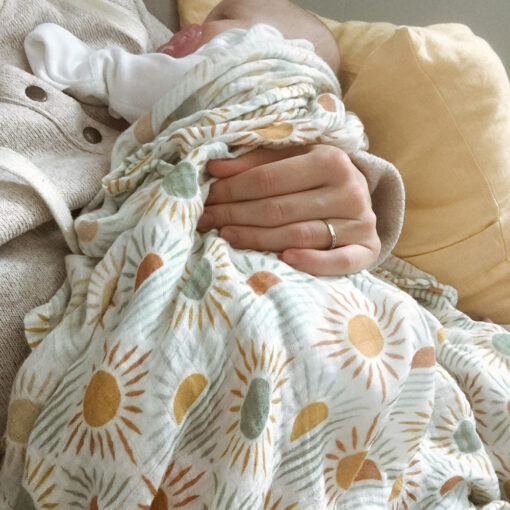 bébé est couché dans les bras de sa maman avec une mousseline à motifs de soleils
