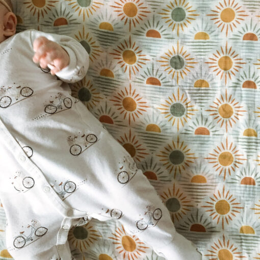 bébé dans un pyjama à motif de vélo couché sur une mousseline à motif de soleils et couchés de soleils
